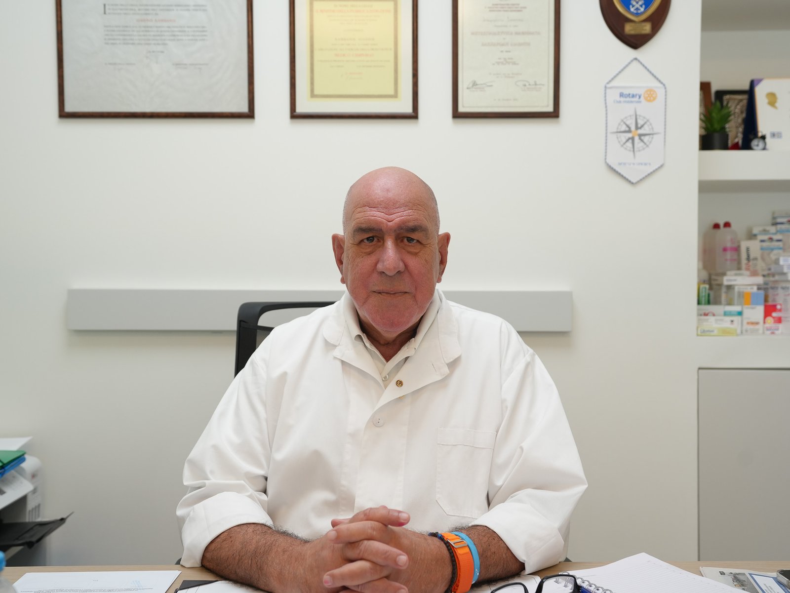 Dr. Ioannis Kambanis at his desk, with framed diplomas and awards on the wall behind him